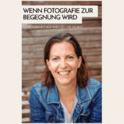 begegnung Porträt der lächelnden Andrea in einer Jeansjacke vor einer Holzwand mit dem Text: Wenn Fotografie zur Begegnung wird – Sichtbarkeit als Weg zu dir selbst.